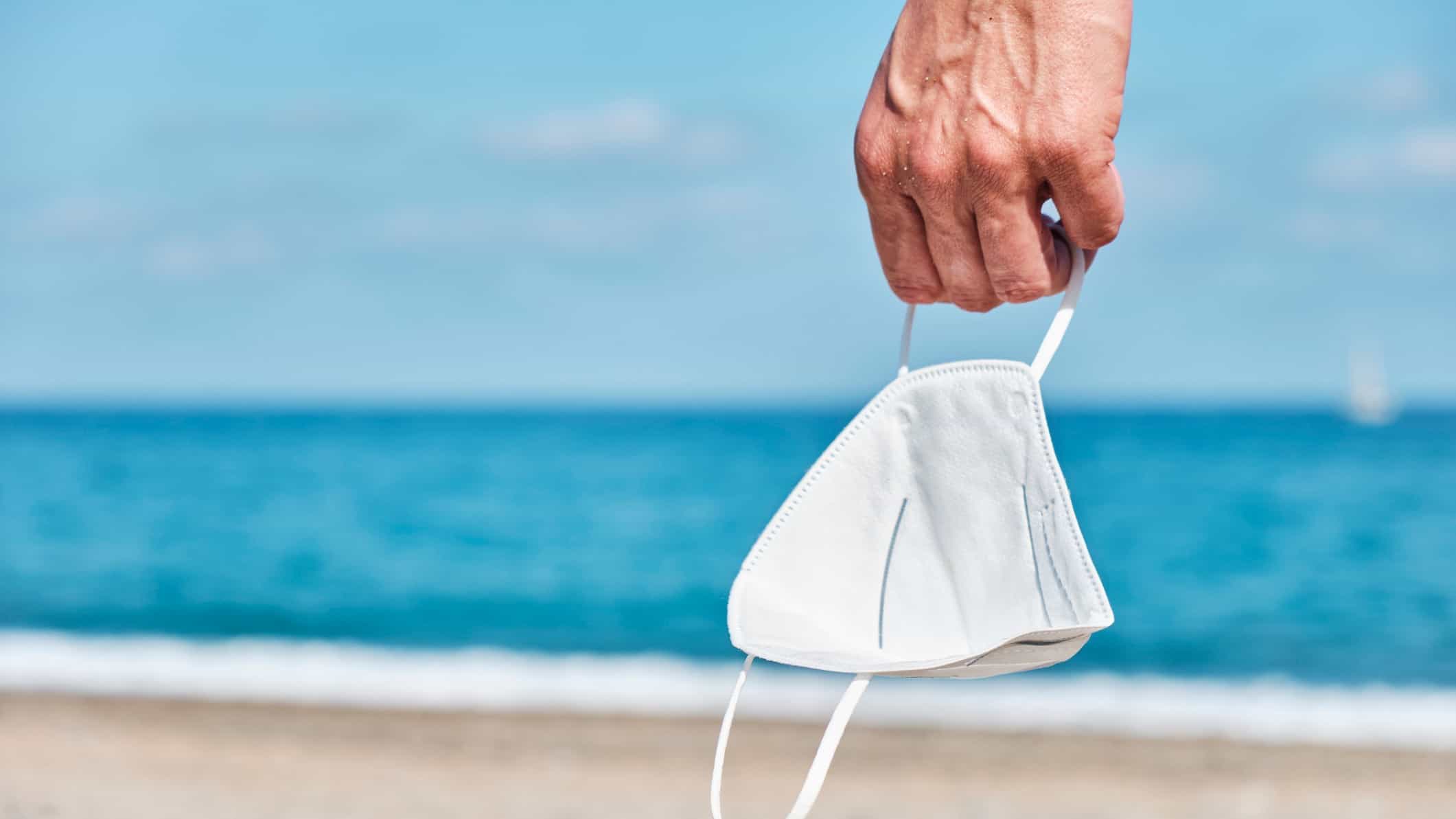 tourism affected by covid represented by hand holding face mask at beach