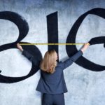 A woman holds a tape measure against a wall painted with the word BIG.