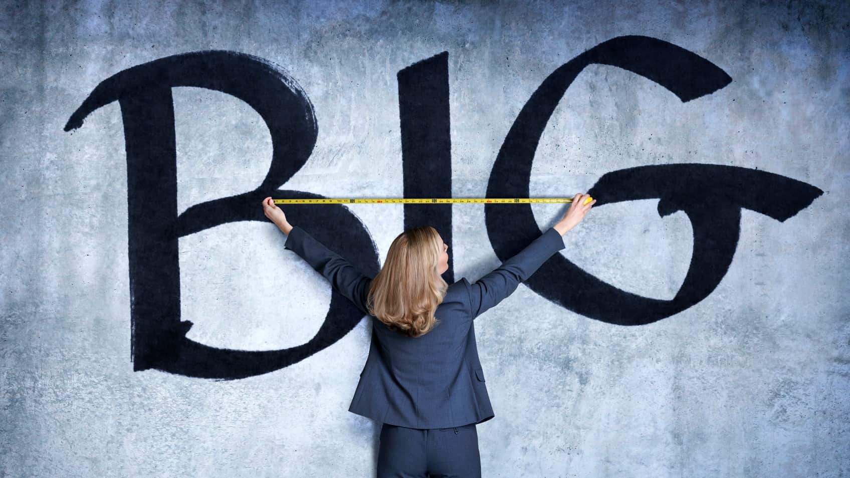 A woman holds a tape measure against a wall painted with the word BIG, indicating a surge in gowth shares