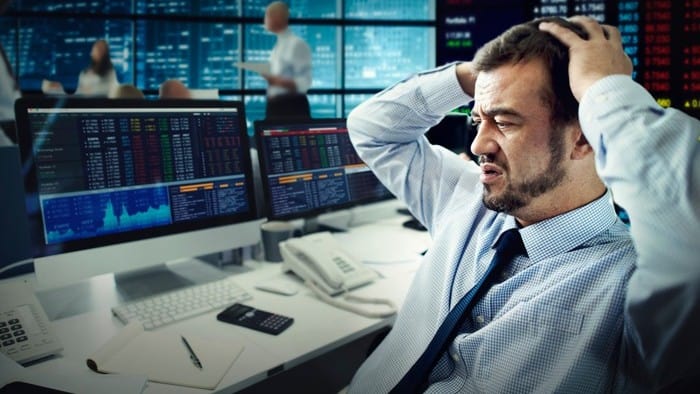 a trader on the stock exchange holds his head in his hands, indicating a share price drop