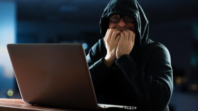 A nervous man dressed in a black hoodie sits at his computer watch to see if his share market gamble pays off, indicatin gthe dark side of the ASX
