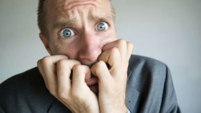 A worried man chews his fingers, indicating a share price crash or drop on the ASX 200