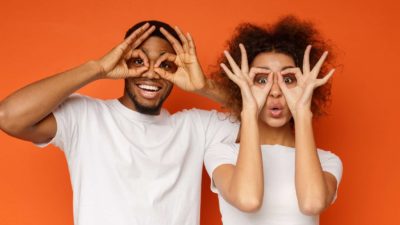 Two happy people use their hands as binoculars, indicating a positive ASX share price or on watch