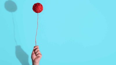 A hand holding a ball of wool up like a red balloon, indicating a riding share price for creative companies