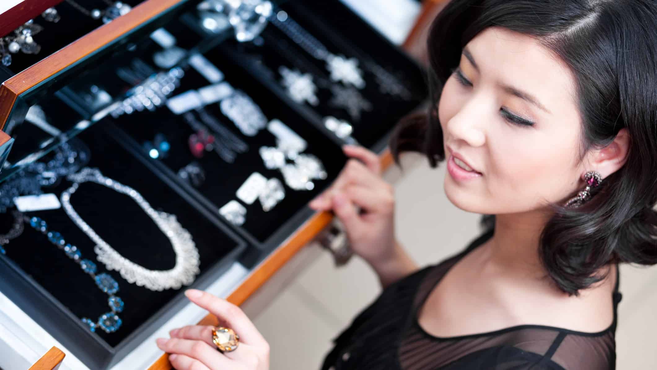 a jewellery store attendant stands at a cabinet displaying opulent necklaces and earrings featuring diamonds and precious stones.