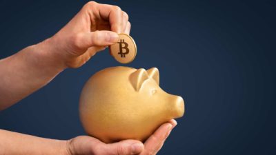 asx share price reacting to bitcoin represented by hand placing bitcoin in gold piggy bank