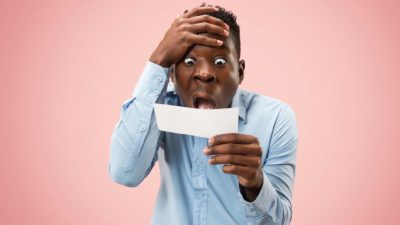 A man holds his head and look in horror at a betting slip, indicating share price drop on the ASX market