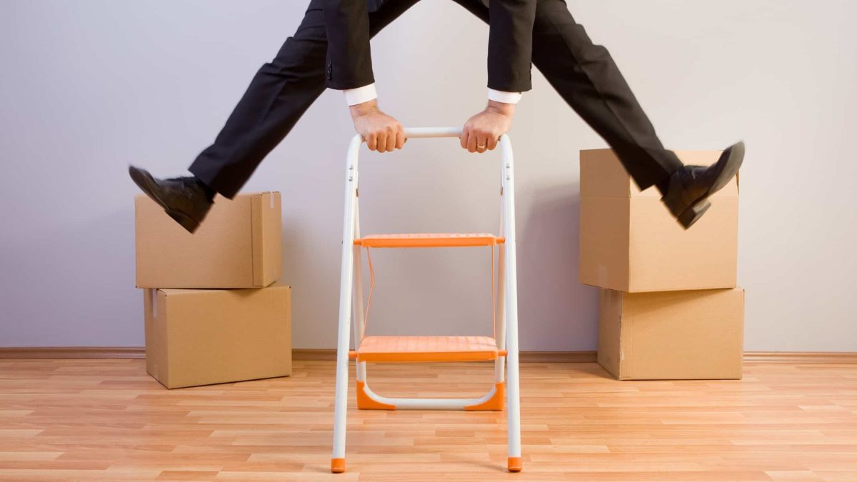 A businessman jumps above a ladder with boxes in the background, indicating a share price rise for packing companies