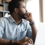 man staring to his left while working on his laptop