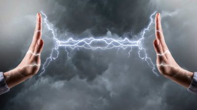 Two hands raised against eachother with lightning flashes between them, indicating and energy clash between fossil fuels and renewables