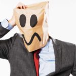 A business man with an idiot face drawn onto a paper bag on his head.