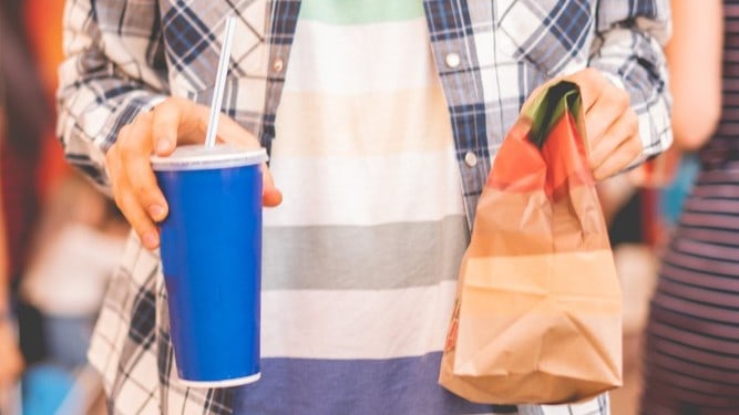 A man carries a bag and drink of McDonald's food as a takeaway