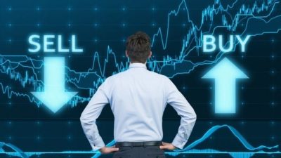 A trader stand looking at a sharemarket graph emblazoned with the words buy and sell