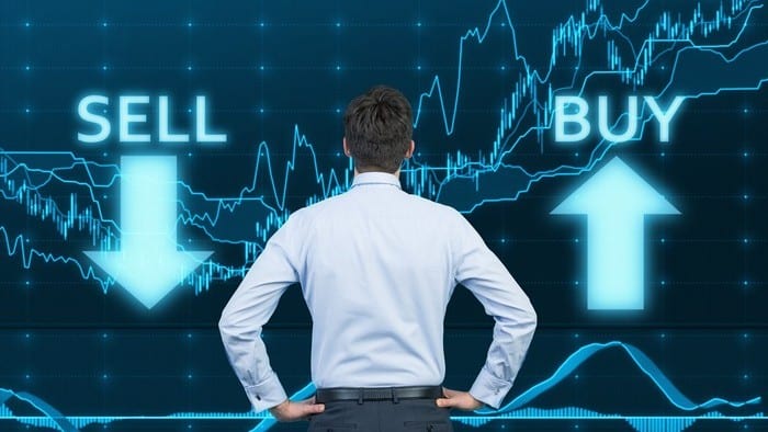A trader stand looking at a sharemarket graph emblazoned with the words buy and sell
