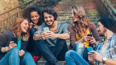 A group of young people smiling and watching TicToc on their mobile phones