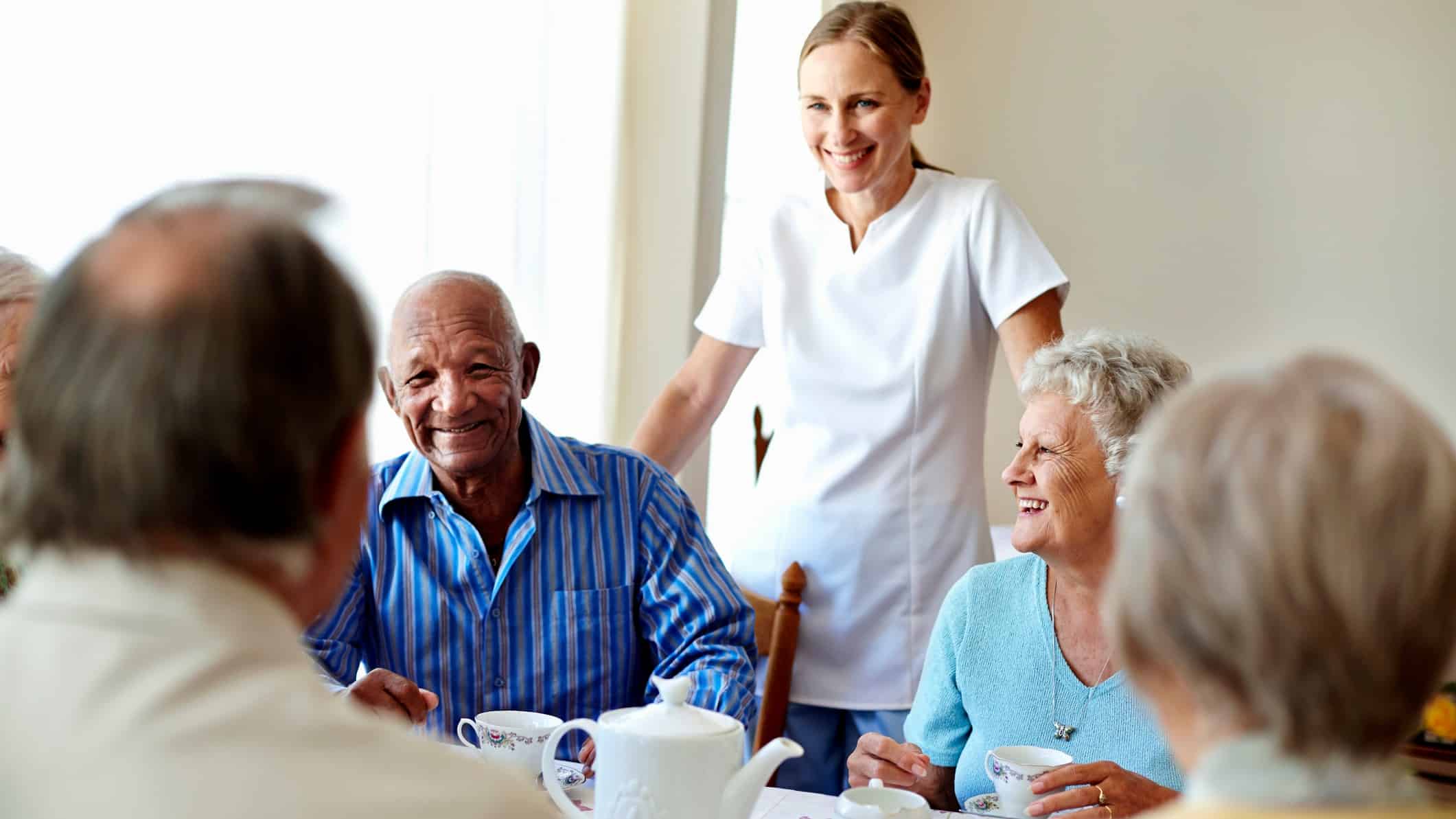 healthcare worker overseeing group of aged care residents at table