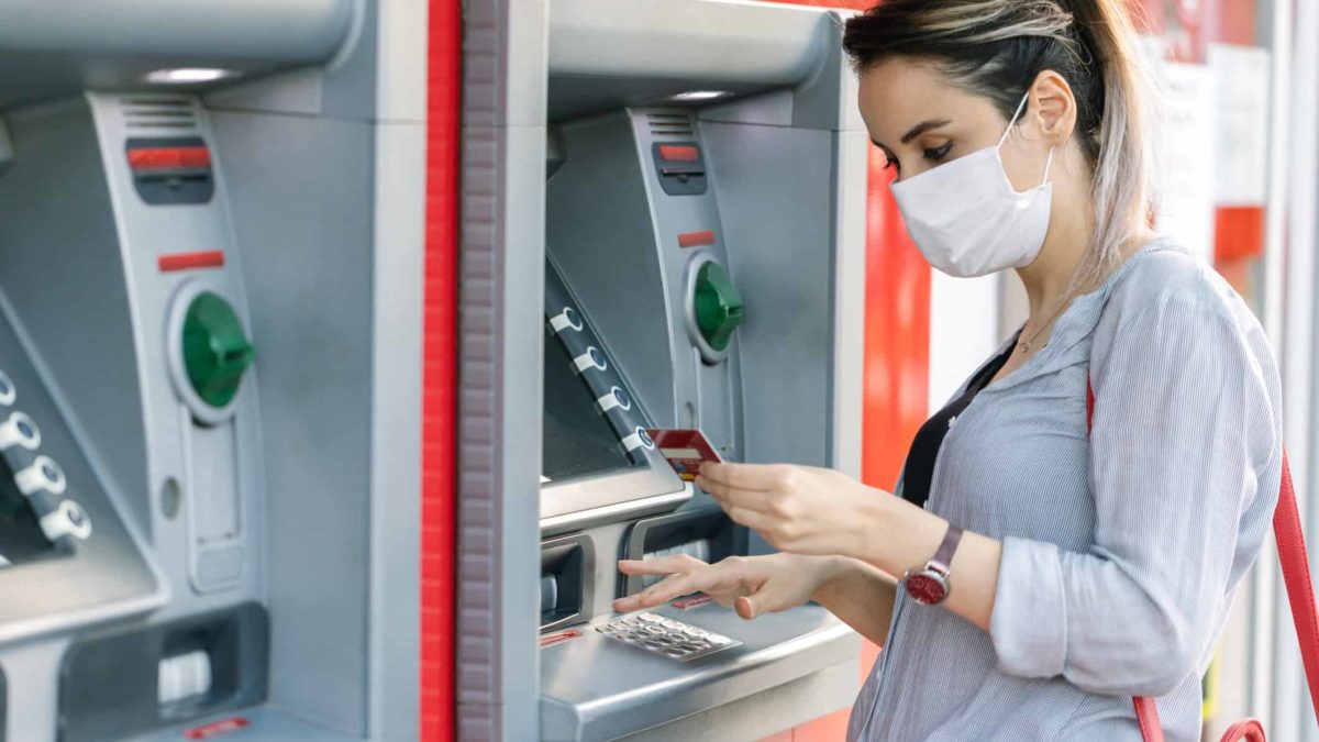 Bank ATM site with a woman in mask looking at her bank card