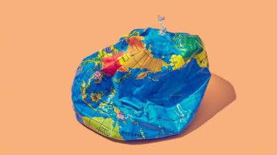 Deflated world globe on peach background to symbolise impact of climate change on the economy