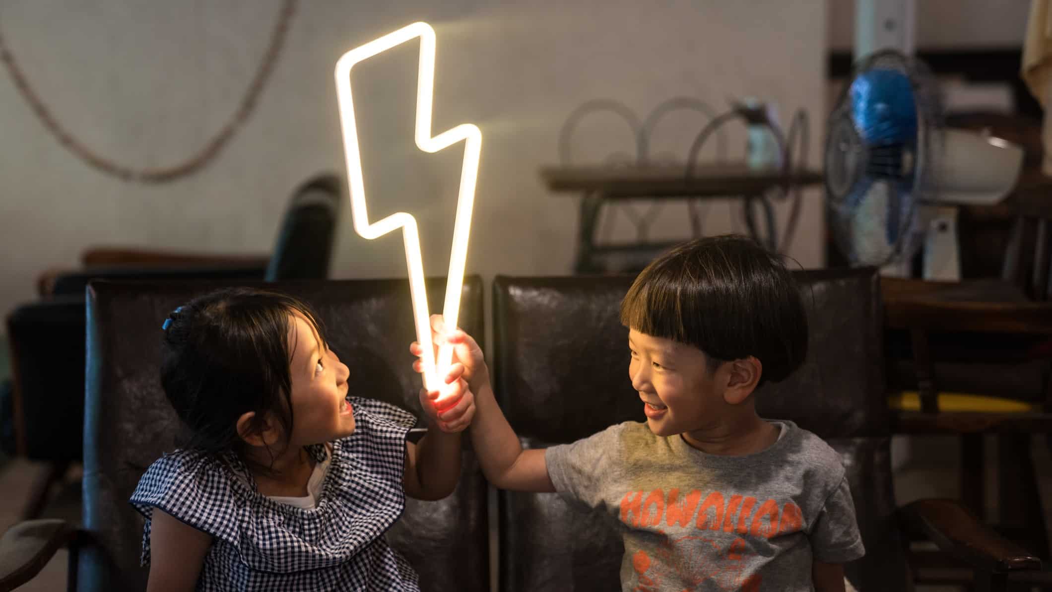Kids holding a lightning bolt light bulb with energy turned on.