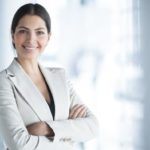 Young female investor in business attire smiling with folded arms.