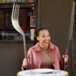 Woman dining at a table with oversized fork and knife in the hospitality industry.