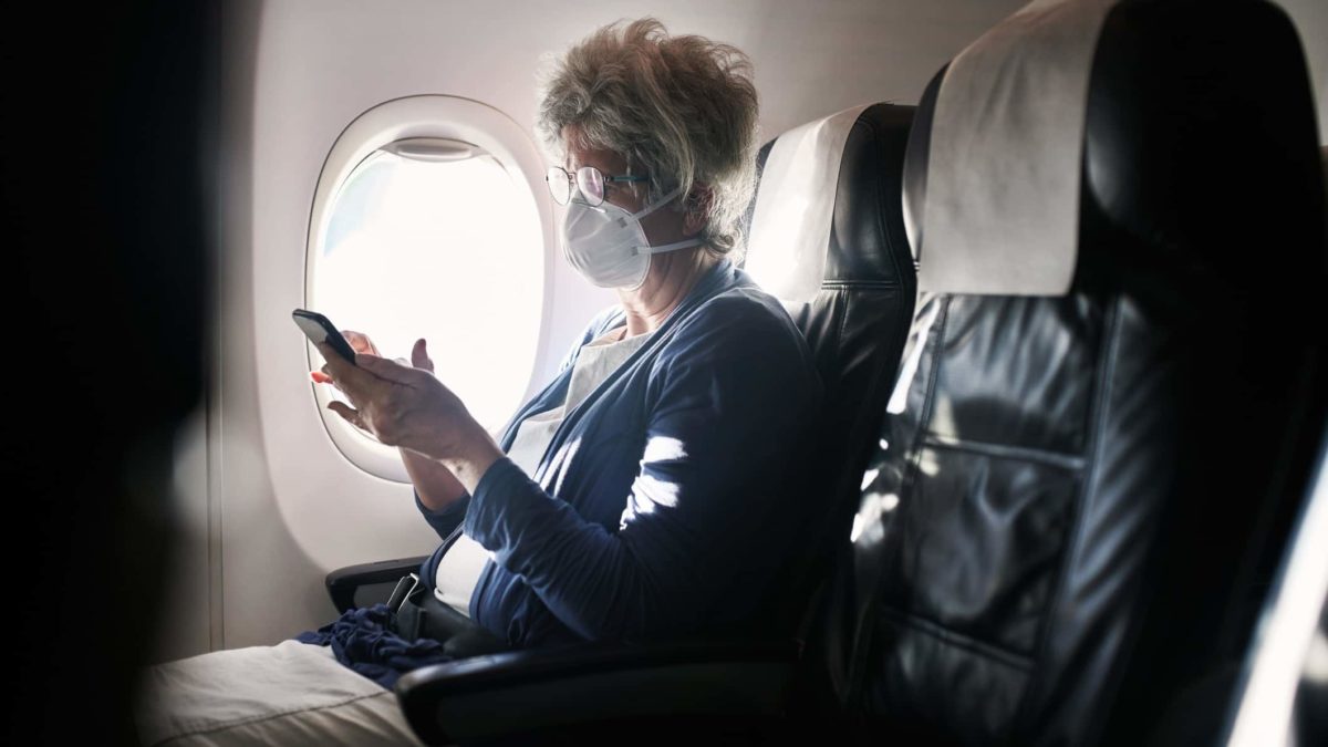 image of a senior woman wearing a mask and using a smartphone in an airplane