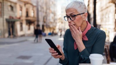 Falling ASX share price represented by woman looking shocked at mobile phone