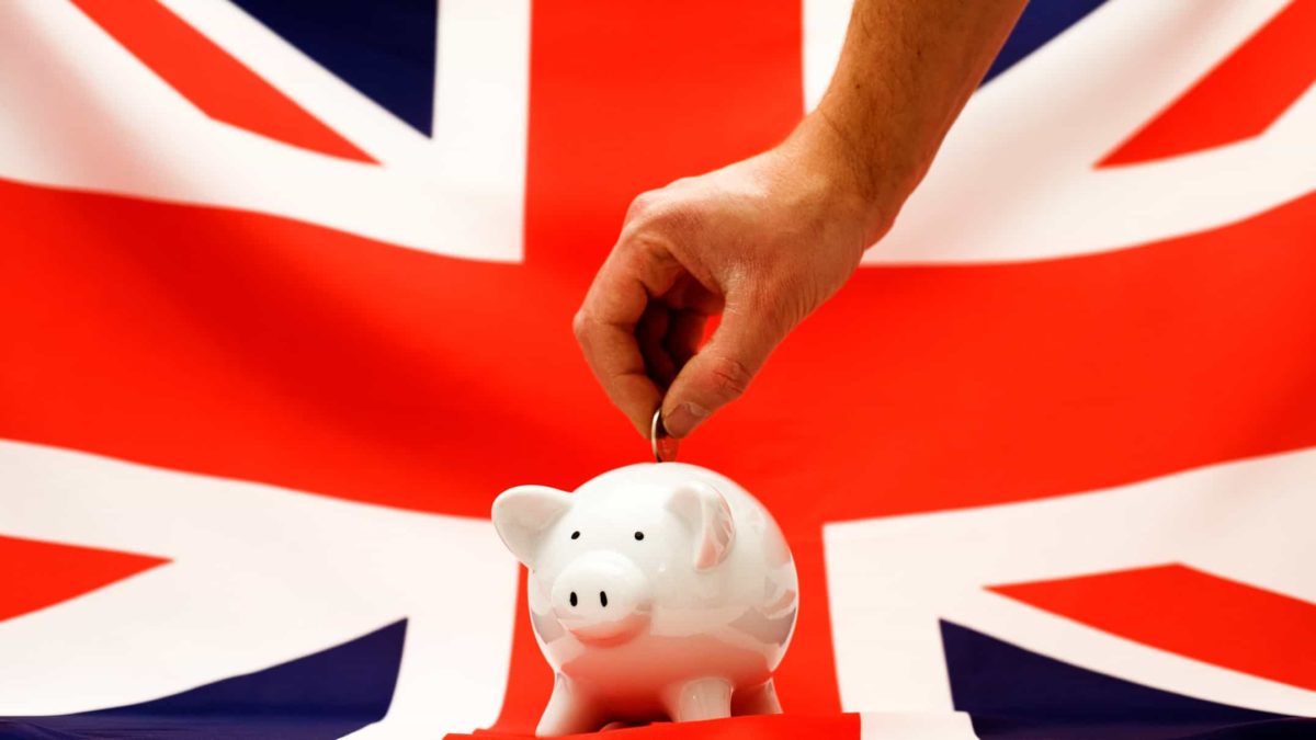 Investing in ftse 100 represented by investor placing money in piggy bank in front of English flag