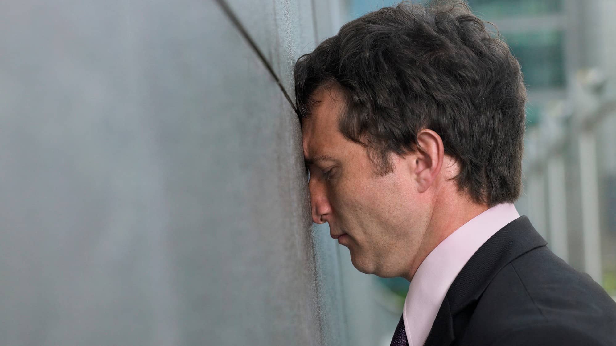 man in business attire with face against wall