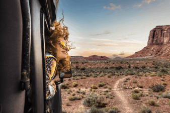 A woman's hair blows wildly as she sticks her head out the train window travelling through the desert.