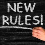 A chalkboard with a hand writing the words New Rules.