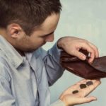 A man shuffles coins out of his empty wallet, indicating there is no shopping money left for retail shares