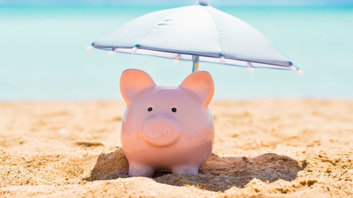 A piggy bank is shaded by a sun umbrella on a beach, indicating a call to protect superannuation savings