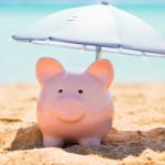 A piggy bank is shaded by a sun umbrella on a beach.