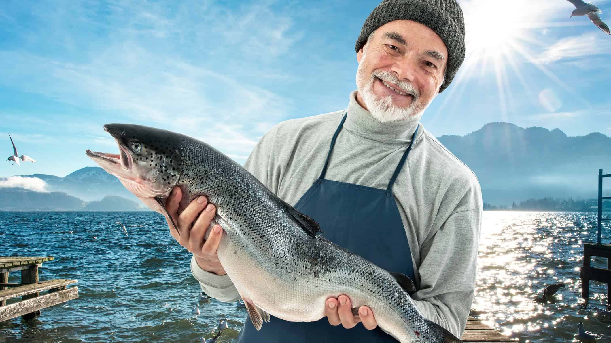 A happy fisherman haldin a large salmon, indicating positive sahre prices news for ASX salmon companies