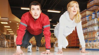 Coles Woolworths supermarket warA man and a woman line up to race through a supermaket, indicating rivalry between the mangorsupermarket shares