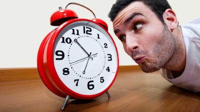 A man closesly watch a clock, indicating a delay or timing issue on an ASX share price movement