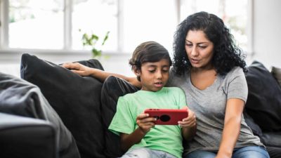 Mother and son sit on couch with son holding a tablet device.