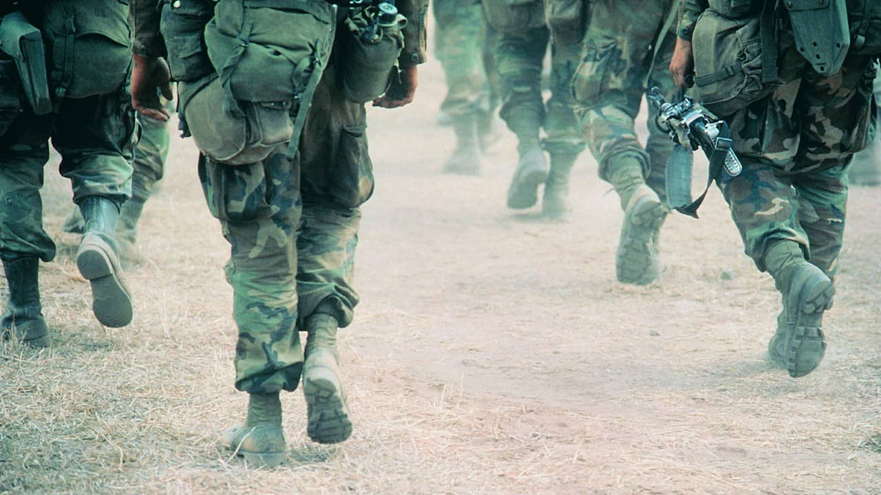 Line of military troops walking on dusty road