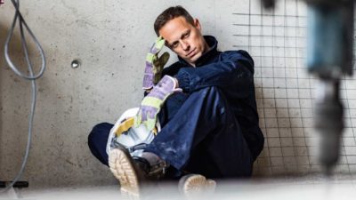 Man in mining or construction uniform sits on the floor with worried look on face