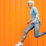 rising asx share price represented by senior lady jumping against orange background