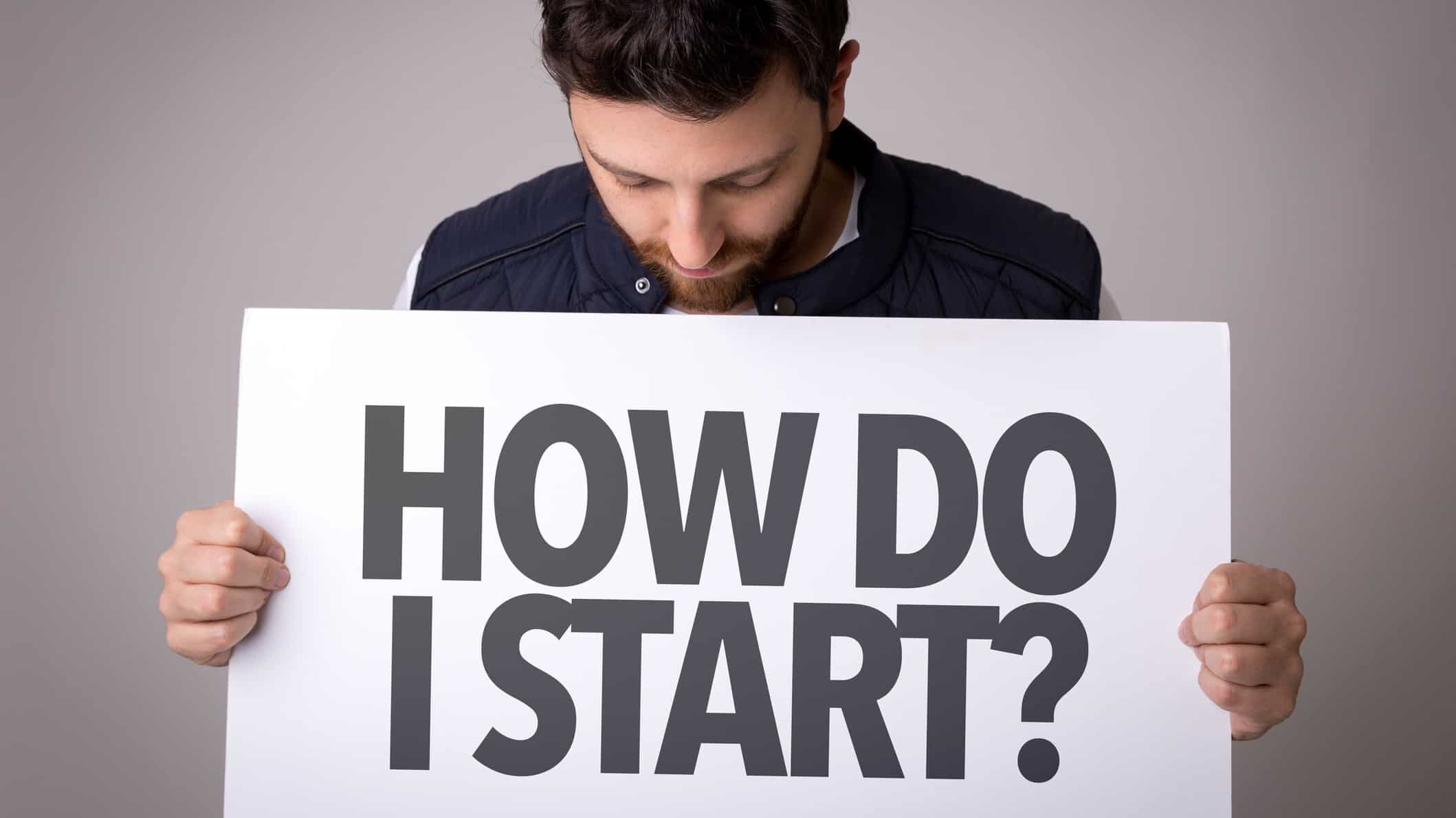 A man holding a sign which says How do I start?, indicating a beginner investor on the ASX