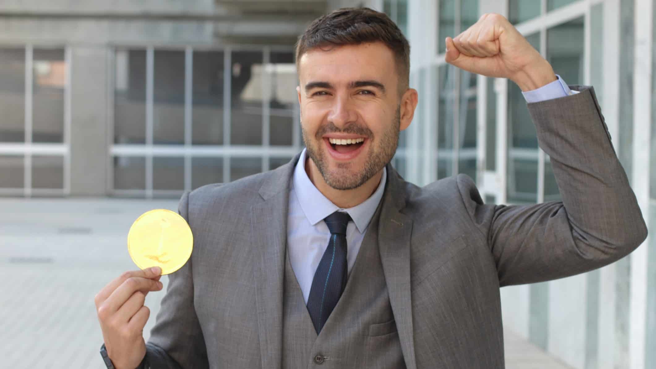 Smiling ASX investor holding a gold bitcoin.
