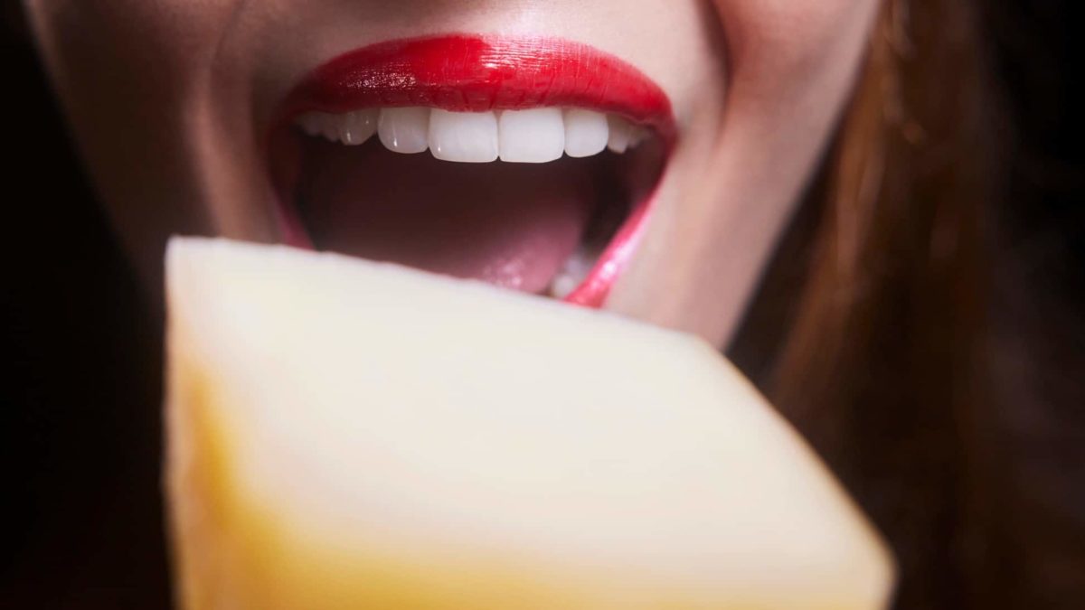 Close-up of a woman taking a big bite out of a block of cheese, indicating a share price rise for ASX cheese companies