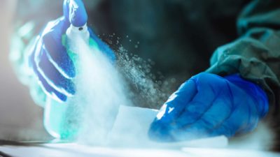 Two hands with gloves spray disinfectant onto a surface, indicating share price movements for ASX biotech companies