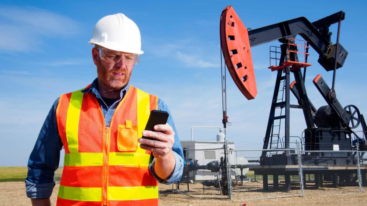 A worried miner looks at his phone in front of a massive drilling, indicating a share price drop for ASX mining companies