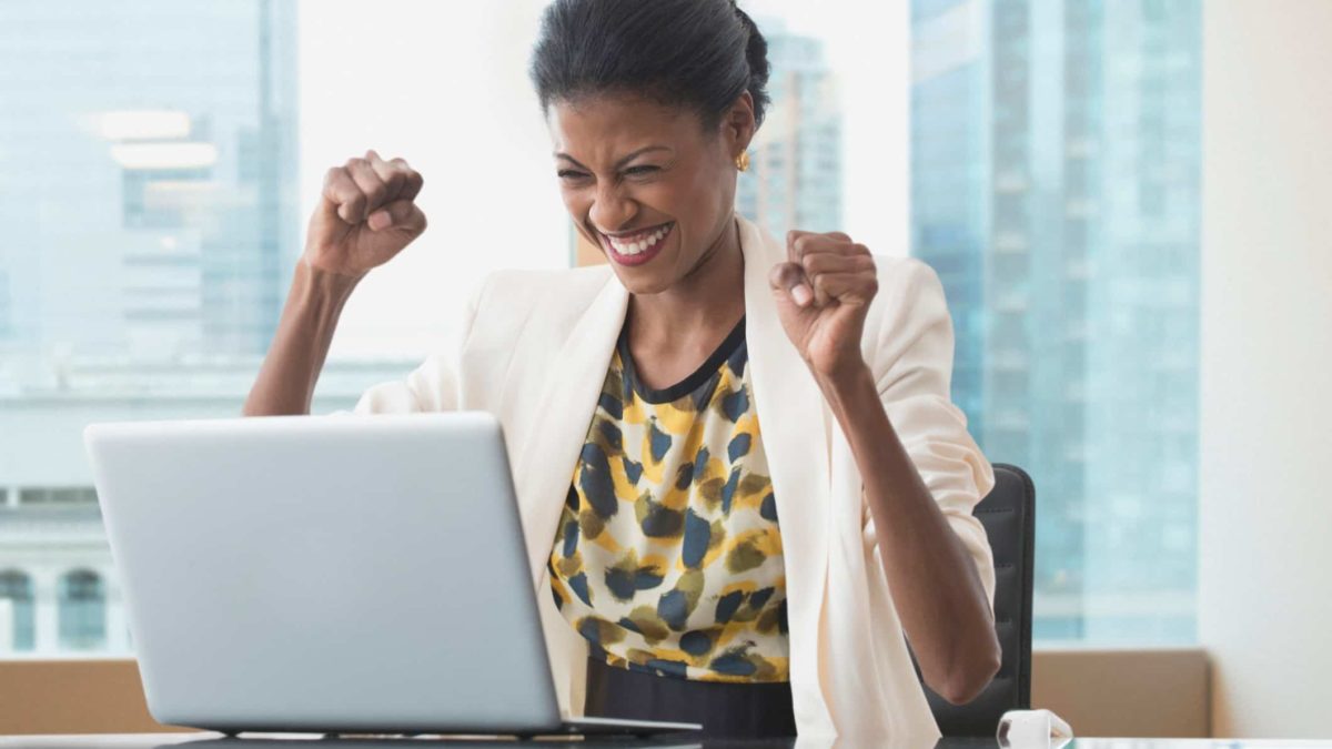 A happy woman at her laptop punches the air, indicating a rising share price