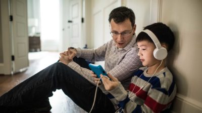 kid with headphones using an electronic device with man looking at it