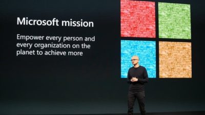 microsoft logo and text in background with a man giving a speech