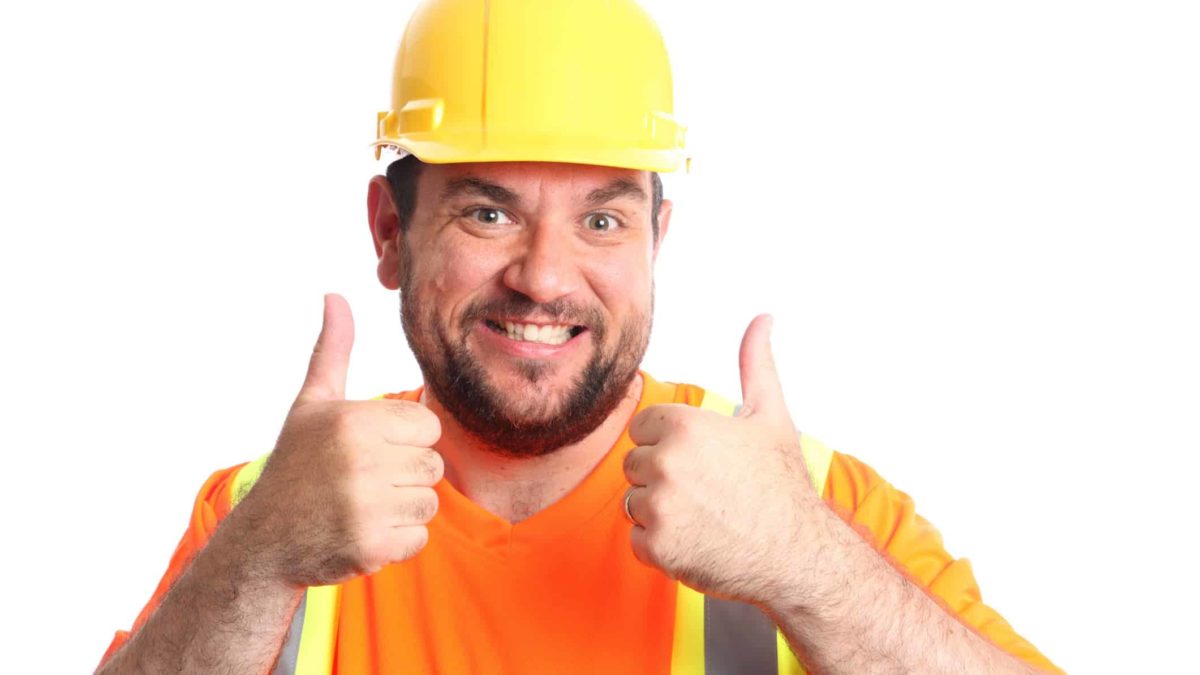 Mining worker wearing hard hat and high vis vest holds thumbs up and smiles